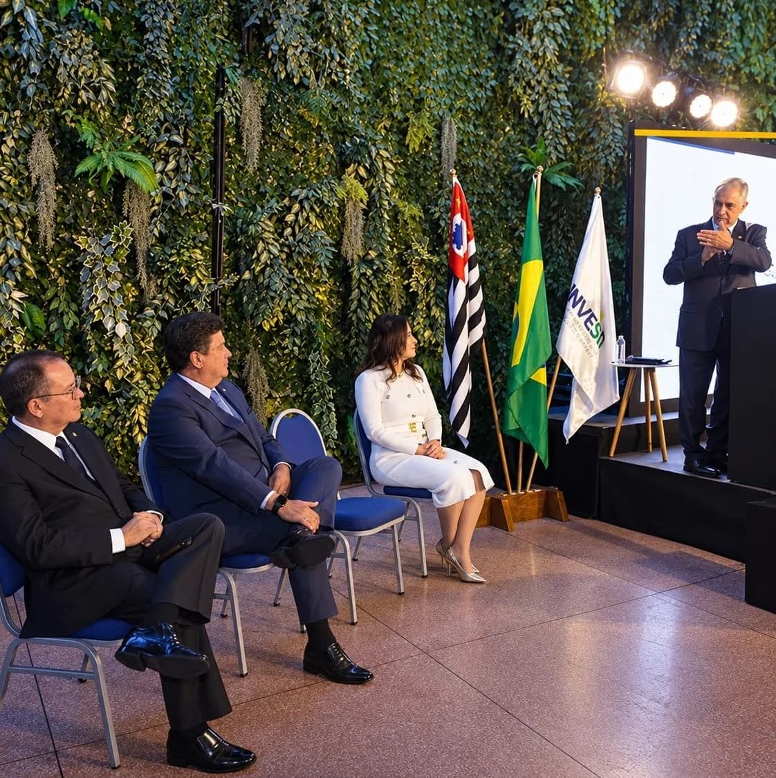 Evento do Instituto InvestBrasil com autoridades sentadas diante das bandeiras de São Paulo, do Brasil e do InvestBrasil